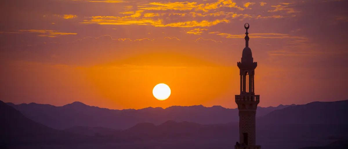 Sonnenuntergang über einer Wüstenlandschaft, rechts das Minarett einer Moschee
