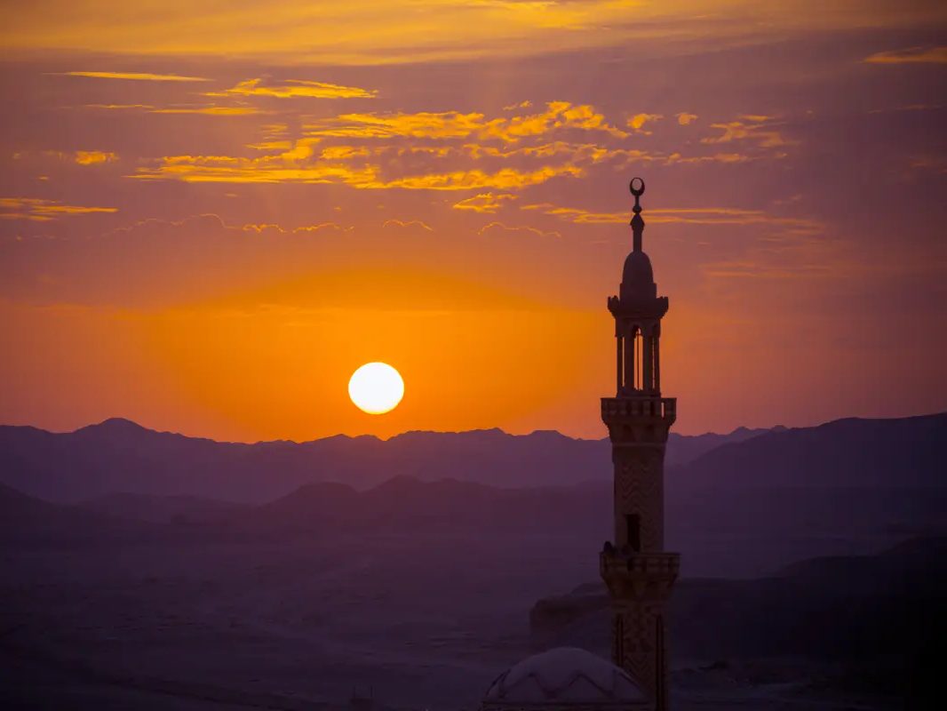 Sonnenuntergang über einer Wüstenlandschaft, rechts das Minarett einer Moschee